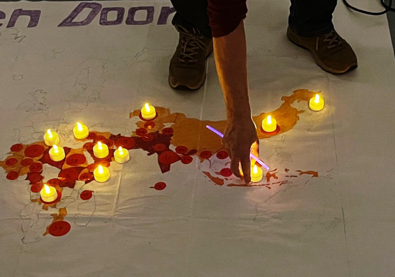 An electronic candle being placed on part of a world map, with certain countries highlighted, laid out on a floor in semi-darkness