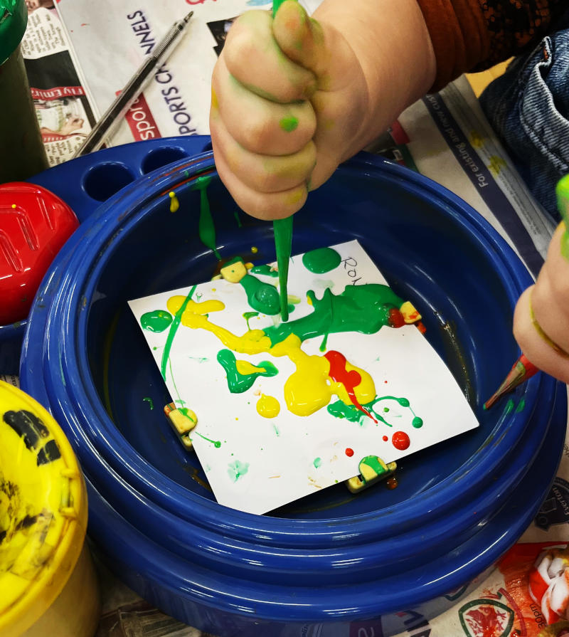 A small child's hands using pipettes to deposit paint on to a square of paper