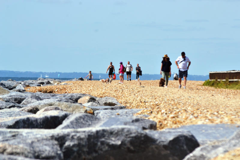 Low-angle view of people walking on shingle beach, with large grey rocks on the foreground