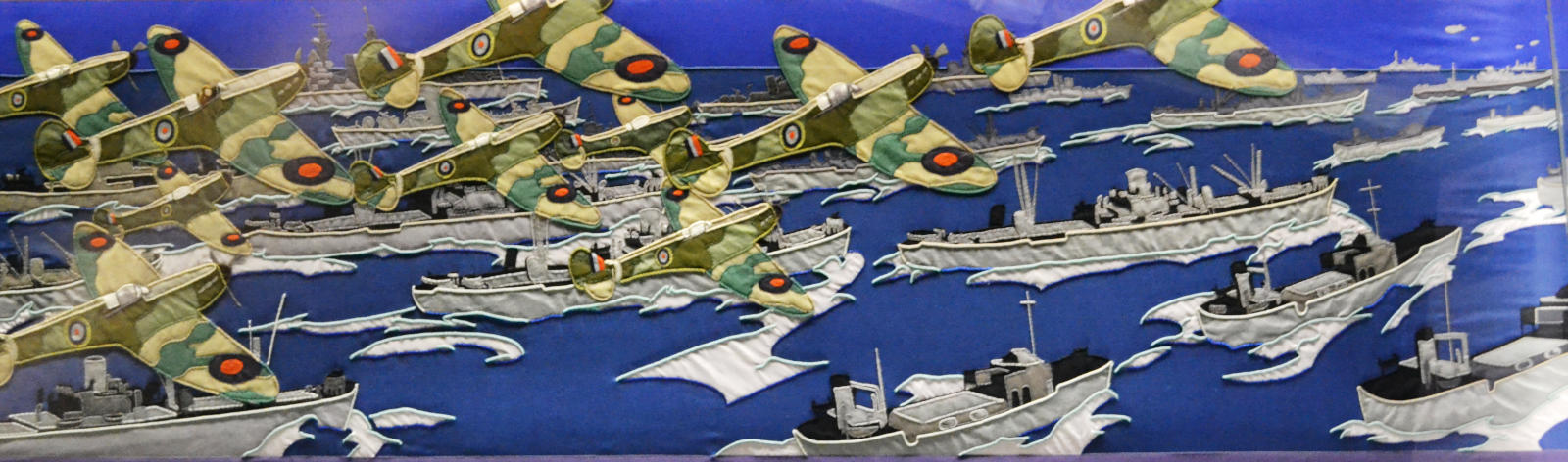 A wide section of tapestry showing a fleet of aircraft in RAF colours in the sky above grey ships on a blue sea