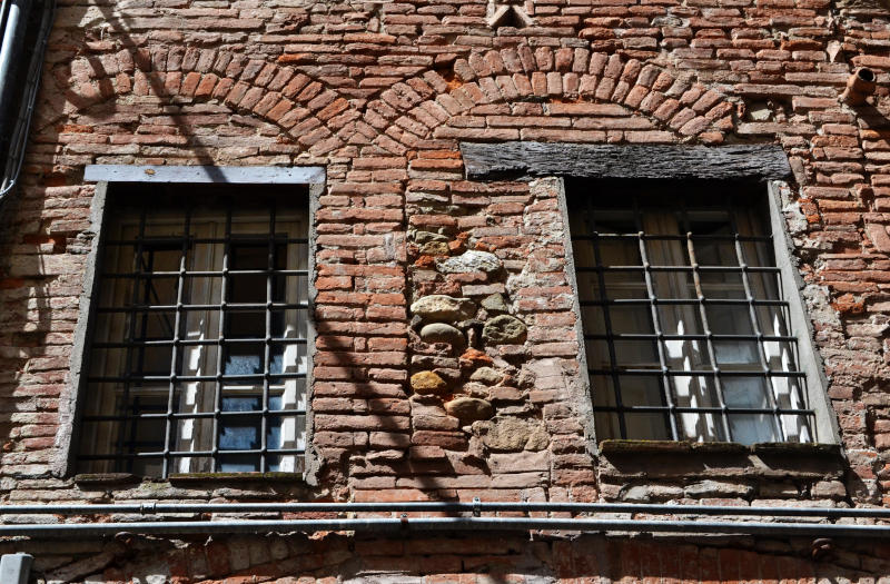 Looking up at an old wall and windows with many styles of brickwork