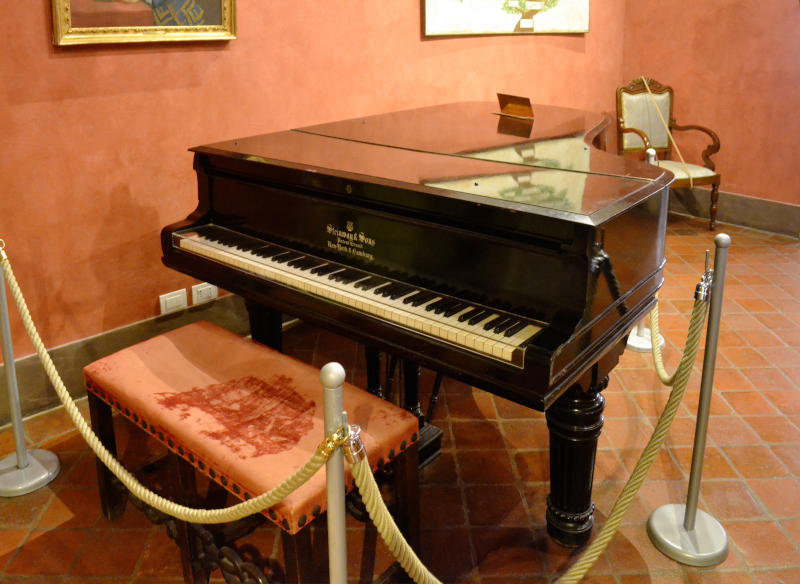 A grand piano in a peach-coloured room, behind a protective rope 