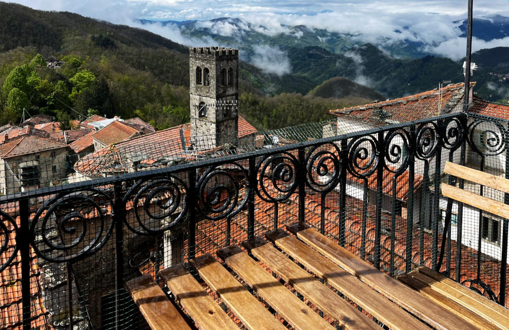 A wooden-floored balcony in the foreground, looking over a church tower and mountains, in sunshine