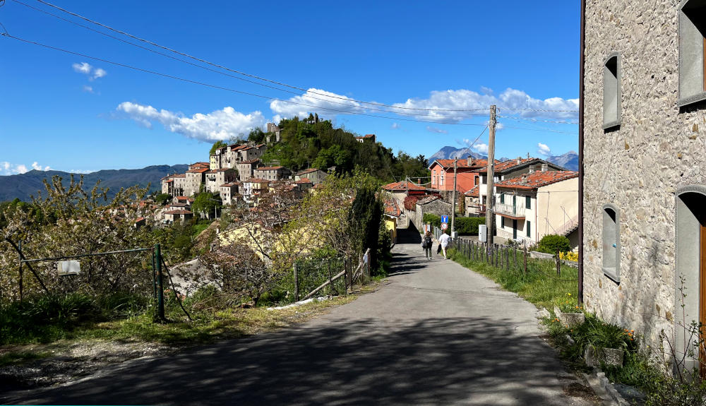 View of a mountain village with a narrow road leading to a cluster of buildings in the distance