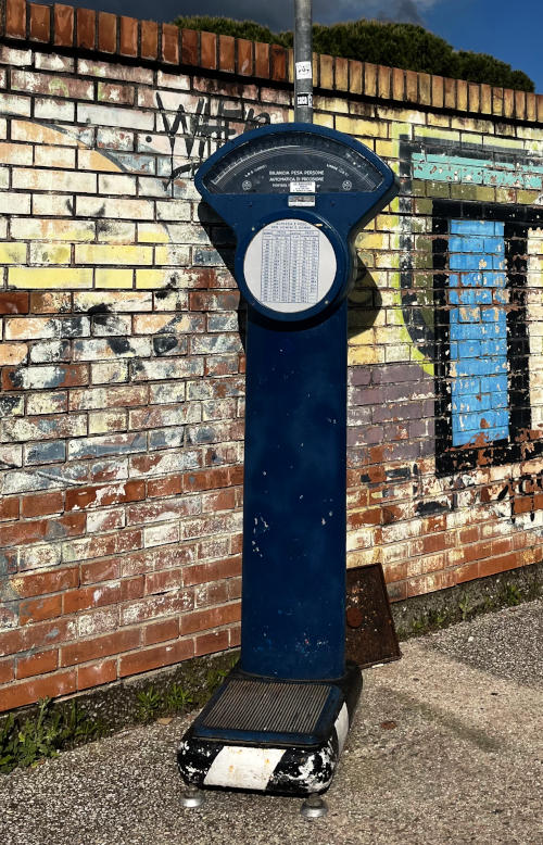 A weighing machine on a pavement in front of a wall