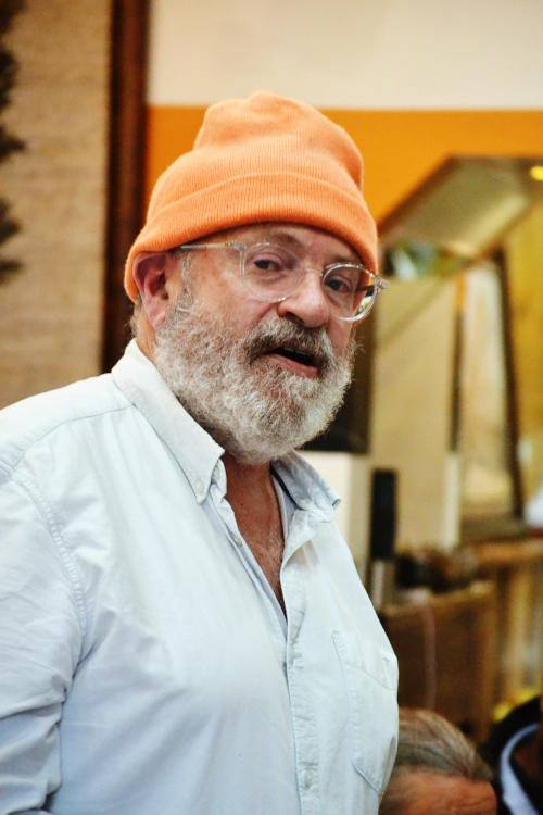 Journalist John Sweeney standing up in a restaurant, wearing an orange woolly hat