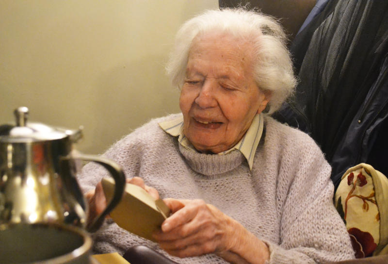 Hanna sitting in an armchair opening an enevelope containing birthday card, with a teapot in the foreground