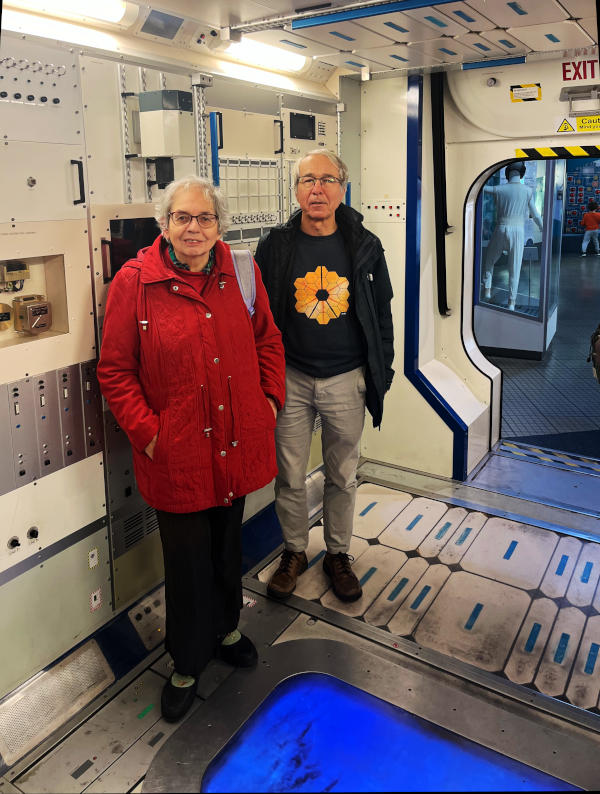 Miriam and Phil inside a mock-up of one of the International Space Station modules. Phil is wearing a sweatshirt with a design of hexagons, the same shape as the James Webb Space Telescope