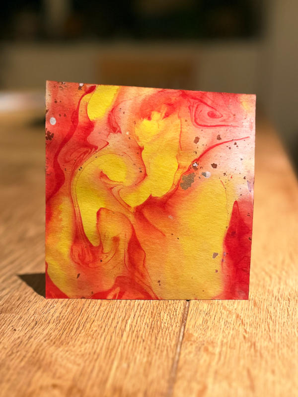 Closeup of a square of paper, with a marbling pattern in orange and yellow